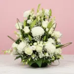 A white flower arrangement in a basket, placed on a table, serving as a condolence basket for a somber occasion.