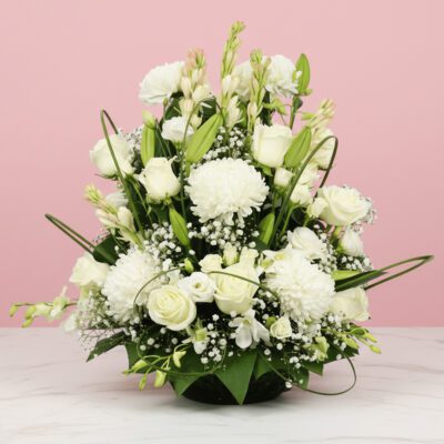 A white flower arrangement in a basket, placed on a table, serving as a condolence basket for a somber occasion.
