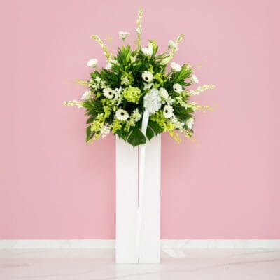 A white stand displaying a delicate arrangement of white sympathy flowers, creating a serene and elegant atmosphere