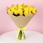 A bouquet of yellow spray roses wrapped in brown paper, showcasing vibrant blooms against a rustic background.