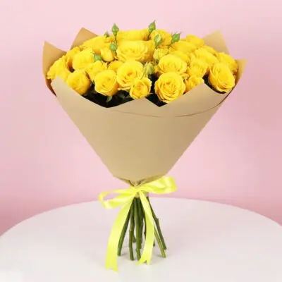 A bouquet of yellow spray roses wrapped in brown paper, showcasing vibrant blooms against a rustic background.