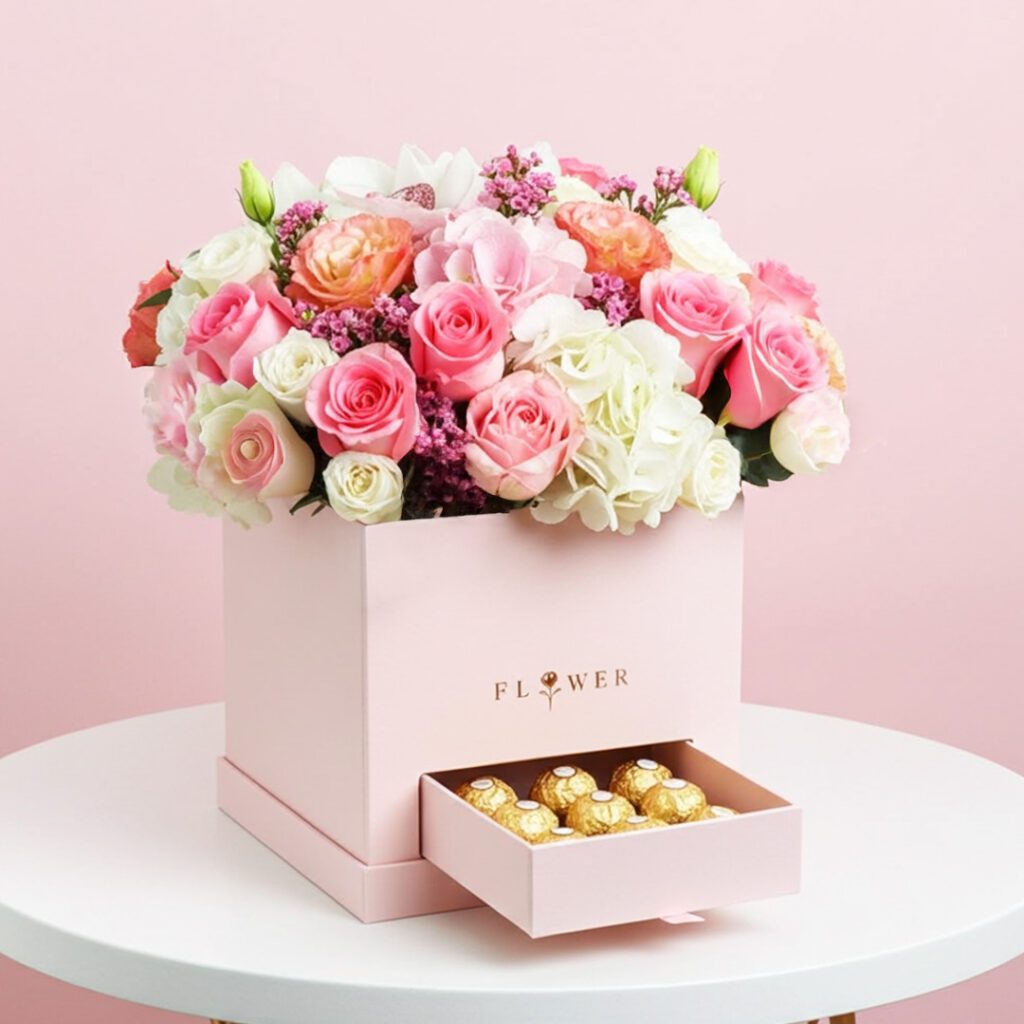 A pink box adorned with flowers and chocolates sits elegantly on a table.