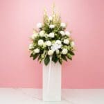 A white vase filled with white flowers and lush greenery, creating a serene and elegant floral sympathy arrangement