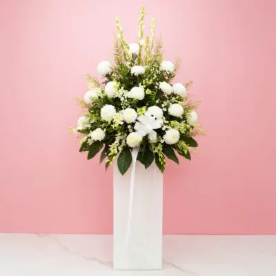 A white vase filled with white flowers and lush greenery, creating a serene and elegant floral sympathy arrangement