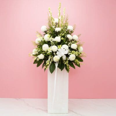A white vase filled with white flowers and lush greenery, creating a serene and elegant floral sympathy arrangement