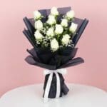 A bouquet of white roses elegantly tied with a black ribbon, showcasing a classic and sophisticated floral arrangement.