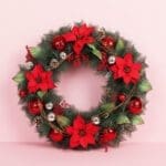 Fresh Christmas wreath adorned with poinsettias and red ornaments, set against a soft pink background.