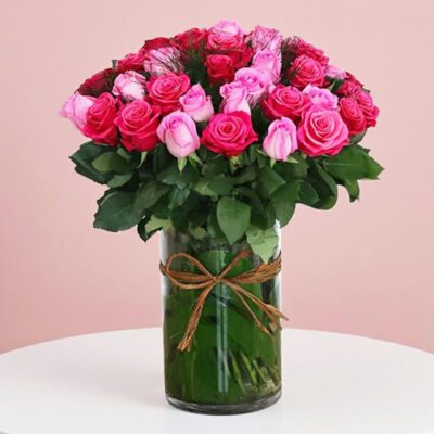 A light vase filled with vibrant pink and red roses, showcasing a beautiful floral arrangement.