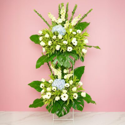 A tall floral funeral flowers arrangement featuring various flowers set against a soft pink background.