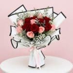 A vibrant bouquet of red and pink roses arranged on a white table, showcasing their lush petals and greenery.