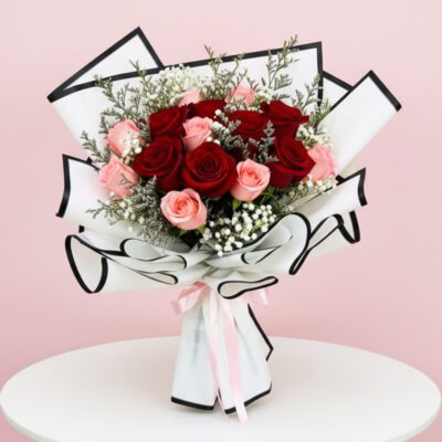 A vibrant bouquet of red and pink roses arranged on a white table, showcasing their lush petals and greenery.