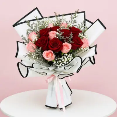 A vibrant bouquet of red and pink roses arranged on a white table, showcasing their lush petals and greenery.