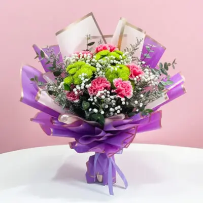 A bouquet featuring purple and pink carnations, button chrysanthemums, and baby's breath, elegantly wrapped in purple.