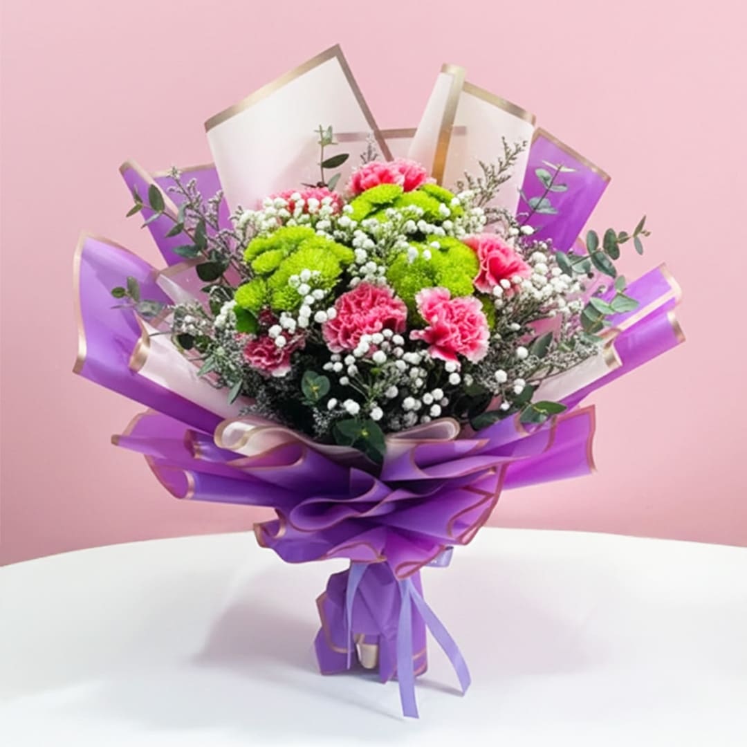 Wrap of Loveliness-01-04-12-25 A bouquet featuring purple and pink carnations, button chrysanthemums, and baby's breath, elegantly wrapped in purple.