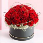 A black box filled with vibrant red roses and delicate white baby's breath flowers.