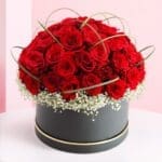 A black box filled with vibrant red roses and delicate white baby's breath flowers.