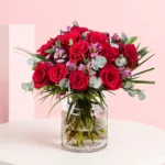 A vase filled with 15 red roses and 5 alstroemerias, showcasing a vibrant floral arrangement.