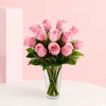 A charming floral arrangement featuring 12 pink roses surrounded by lush greenery, exuding elegance and sweetness.