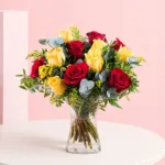 A cylinder vase filled with six yellow and six red roses, showcasing a vibrant floral arrangement.