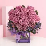 Beautiful Lavender Love Rose arrangement in a glass vase, combining purple roses, wax flowers, and caspia for sophistication.