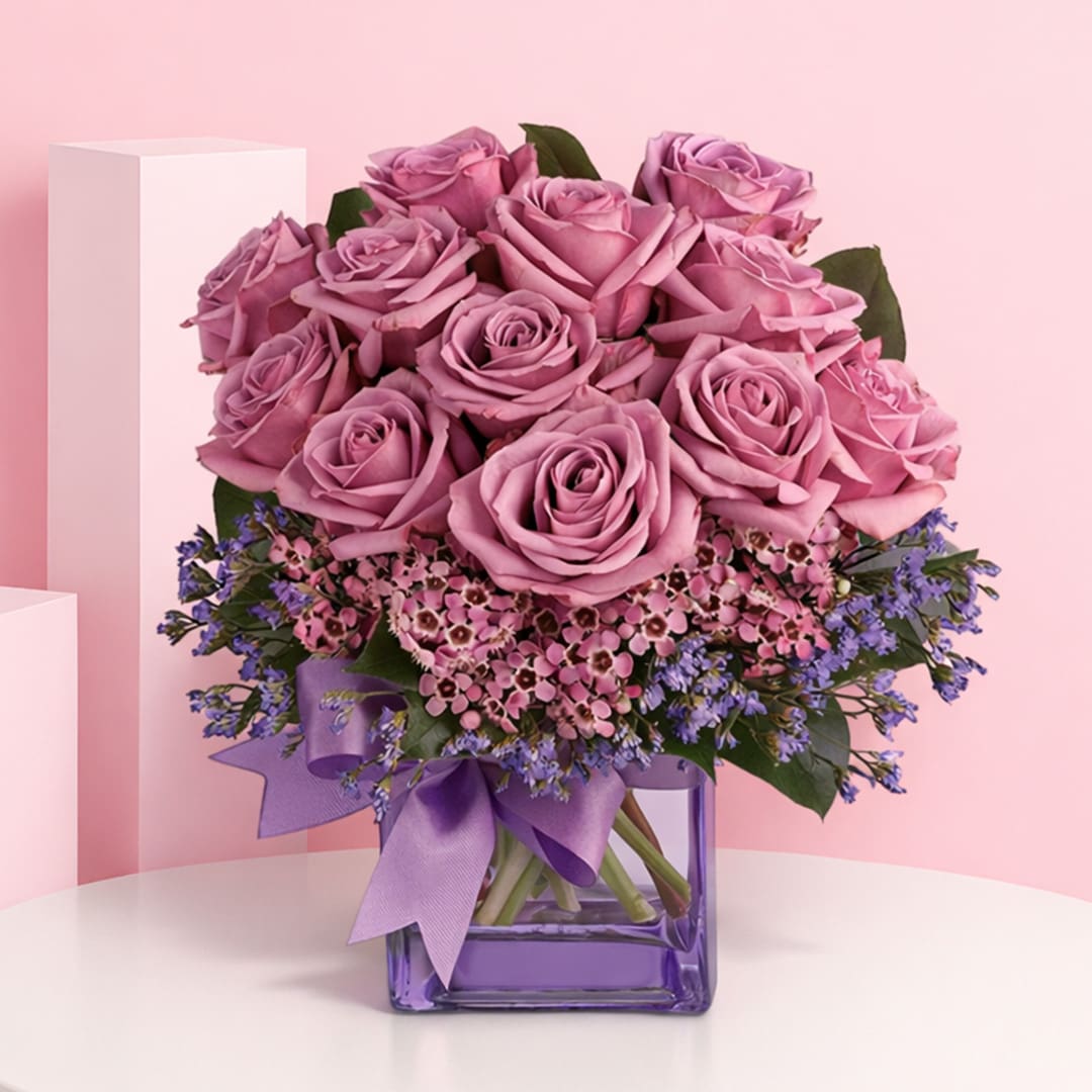lavender-love-rose-in-designer-vase-2026 Beautiful Lavender Love Rose arrangement in a glass vase, combining purple roses, wax flowers, and caspia for sophistication.