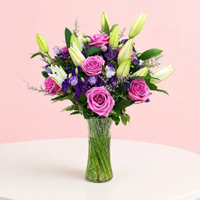A lavish vase arrangement featuring 5 purple roses, 5 lilies, 3 purple eustoma, 5 statice, and lush greenery.