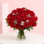 A bouquet of 35 red roses arranged in a clear cylinder vase, showcasing vibrant blooms and lush green leaves.
