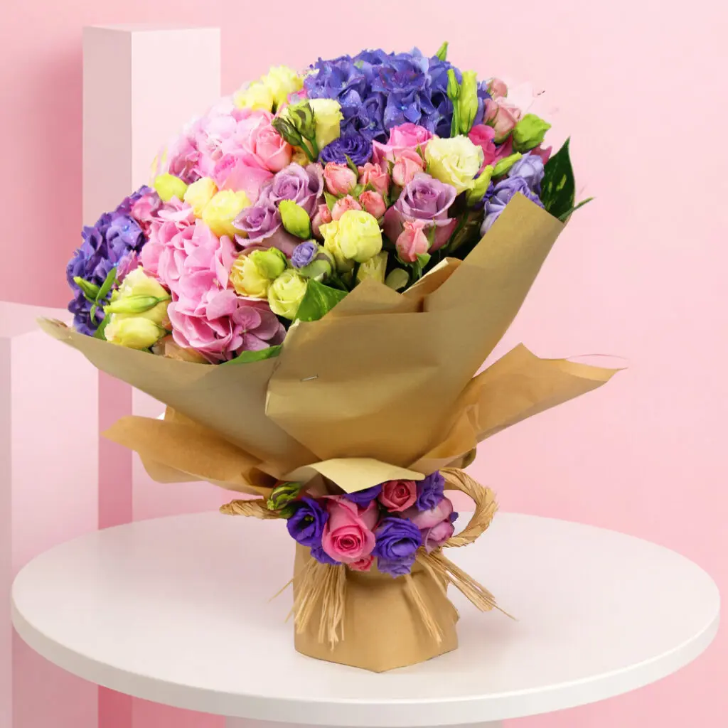 A vibrant bouquet featuring pink, light yellow, and purple spray roses, complemented by pink and purple hydrangeas.