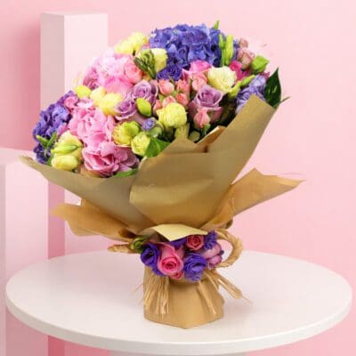 A vibrant bouquet featuring pink, light yellow, and purple spray roses, complemented by pink and purple hydrangeas.