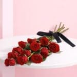 A hand-tied bouquet of 12 vibrant red roses adorned with a black ribbon.