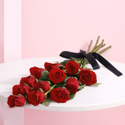 A hand-tied bouquet of 12 vibrant red roses adorned with a black ribbon.