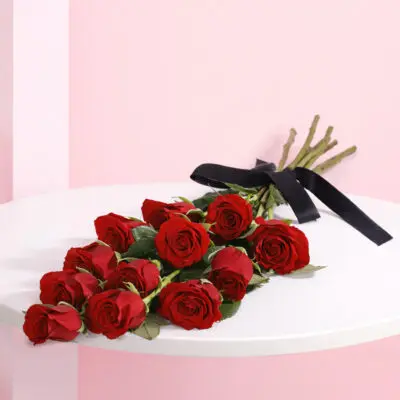A hand-tied bouquet of 12 vibrant red roses adorned with a black ribbon.