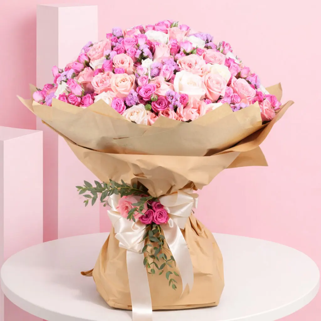 A bouquet of pink spray roses and purple roses arranged in a brown paper bag.