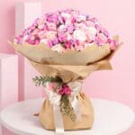 A bouquet of pink spray roses and purple roses arranged in a brown paper bag.