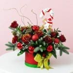 A festive Christmas arrangement featuring red and green decorations, including a candy cane, in a decorative box.