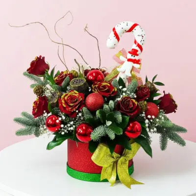 A festive Christmas arrangement featuring red and green decorations, including a candy cane, in a decorative box.