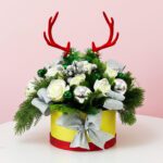 A holiday centerpiece with a bouquet of green leaves and deer antlers, arranged beautifully in a decorative box.