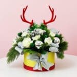 A holiday centerpiece with a bouquet of green leaves and deer antlers, arranged beautifully in a decorative box.
