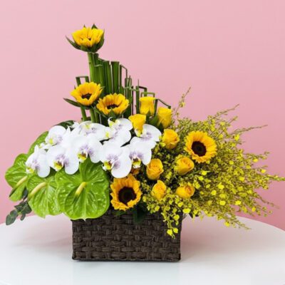 A woven basket filled with vibrant yellow flowers and delicate orchids, showcasing a cheerful floral arrangement.