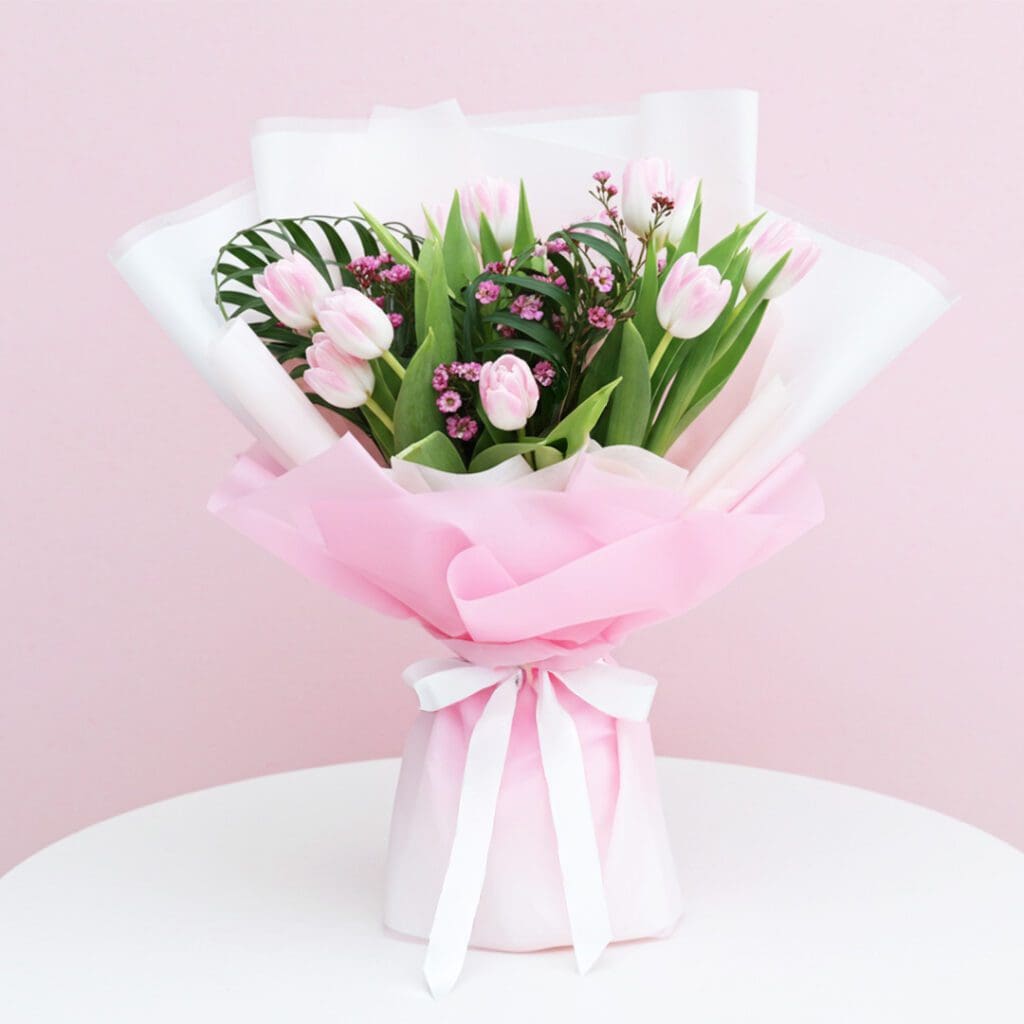 A bouquet of pink tulips tied with a white ribbon, showcasing vibrant flowers against a soft background.