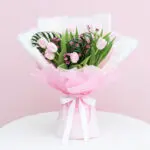 A bouquet of pink tulips tied with a white ribbon, showcasing vibrant flowers against a soft background.