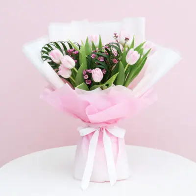 A bouquet of pink tulips tied with a white ribbon, showcasing vibrant flowers against a soft background.