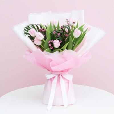 A bouquet of pink tulips tied with a white ribbon, showcasing vibrant flowers against a soft background.