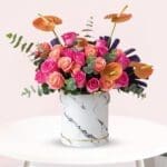 A bouquet of pink and orange roses arranged in a sleek marble vase.