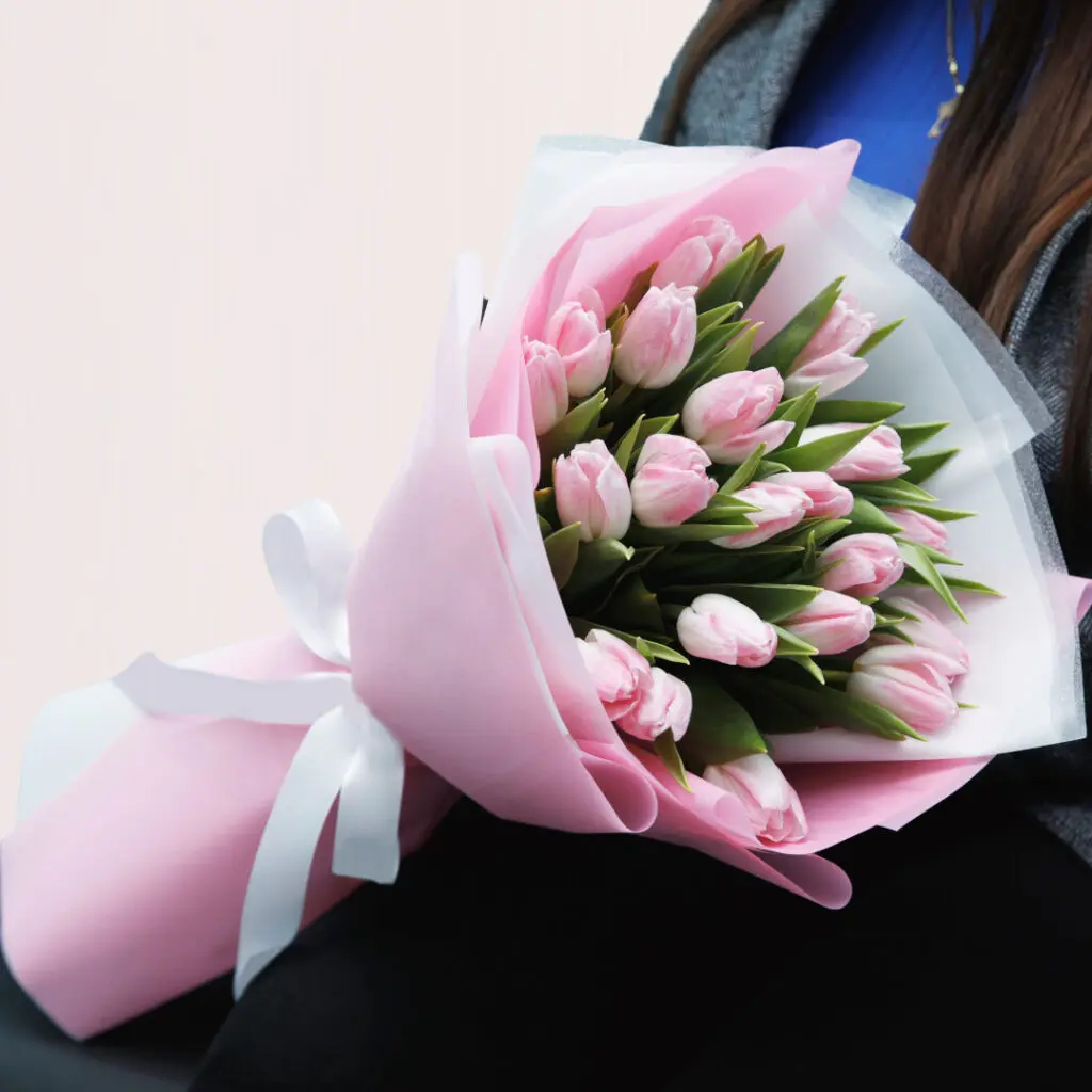 A woman smiling while holding a vibrant bouquet of pink tulips in her hands