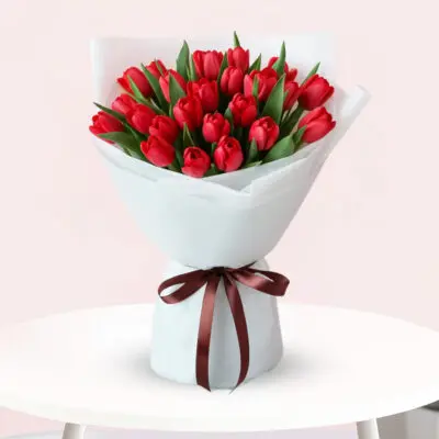 A vibrant bouquet of red tulips tied with a brown ribbon, showcasing their fresh blooms and elegant arrangement.