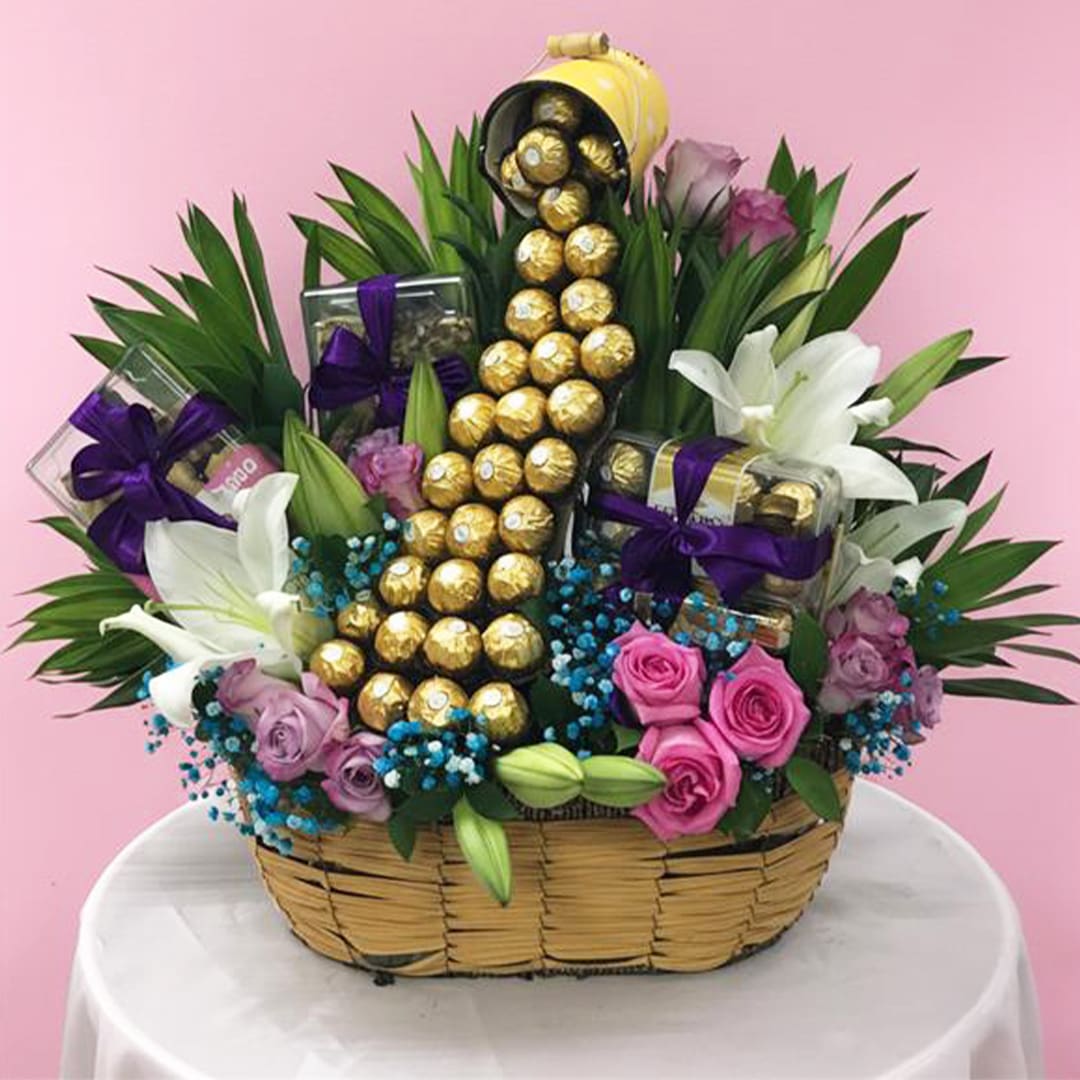 Token of love-15-10 A basket overflowing with assorted chocolates and vibrant flowers, creating a delightful and colorful arrangement.