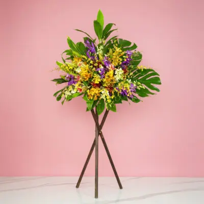 A Grand Opening Orchid Mix And Casa Lily Flowers On A Stand, Set Against A Pink Wall.