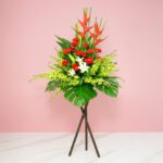 A Vibrant Flower Arrangement On A Stand Featuring Red And White Gerberas, Casa Lilies, Orchids, And Seasonal Greenery.