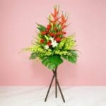 A Vibrant Flower Arrangement On A Stand Featuring Red And White Gerberas, Casa Lilies, Orchids, And Seasonal Greenery.